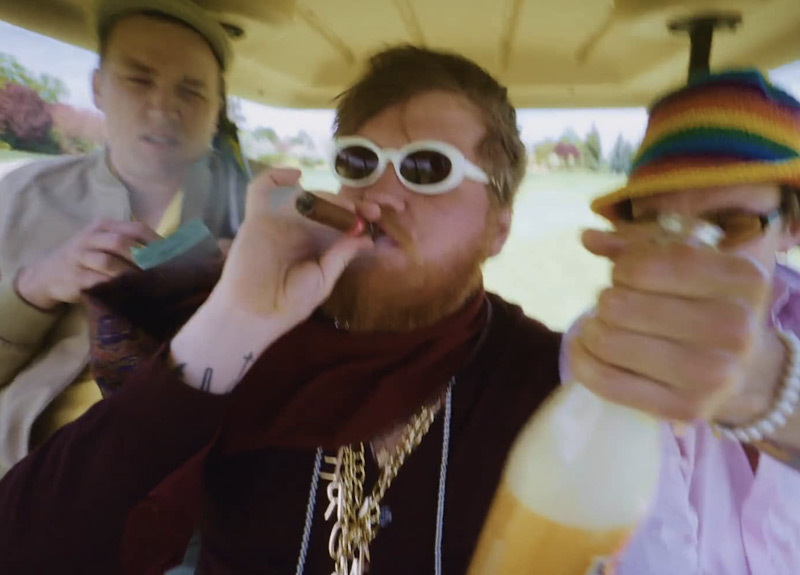 three guys sitting in golf cart, drinking champagne and smoking a cigar
